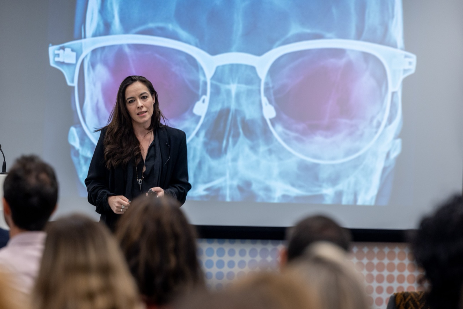 Katherine Templar Lewis on stage in front of an X-ray of a skull wearing glasses